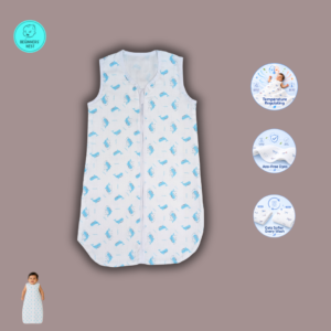 A smiling South Asian baby lies on a soft beige blanket wearing a lightweight white muslin sleeping bag with a front zipper and a small blue whale. The sleeveless sleeping bag has a slim, straight silhouette with a rounded bottom, while the baby's arms rest comfortably at the sides in a bright, softly lit overhead photograph.